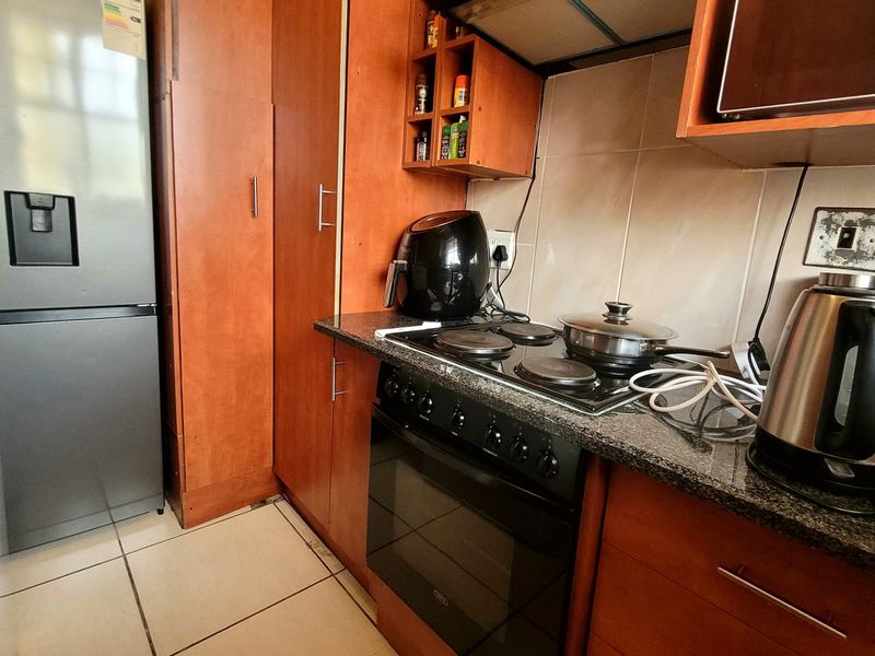 A functional kitchen featuring wood-finish cabinetry, granite countertops, a built-in oven with electric hob, and tiled flooring.