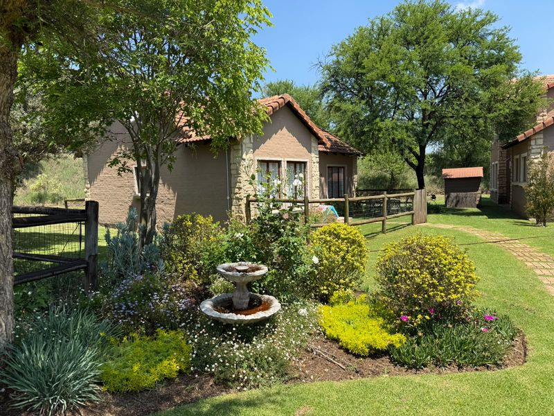 A well-maintained rear garden area featuring stone-clad exterior walls, a tiled roof, brick pathways, and established landscaping with a central water feature.