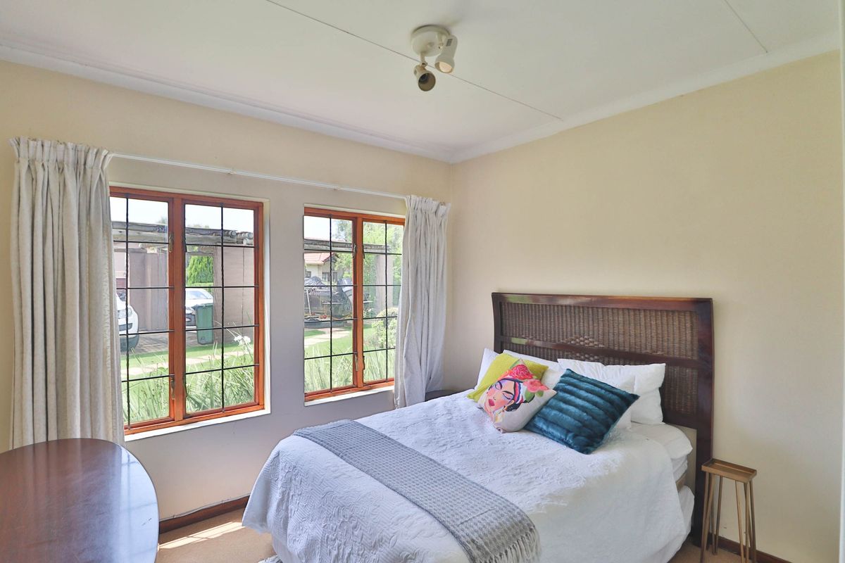 A well-lit bedroom featuring timber-framed windows with security bars, neutral wall finishes, and classic ceiling cornicing.
