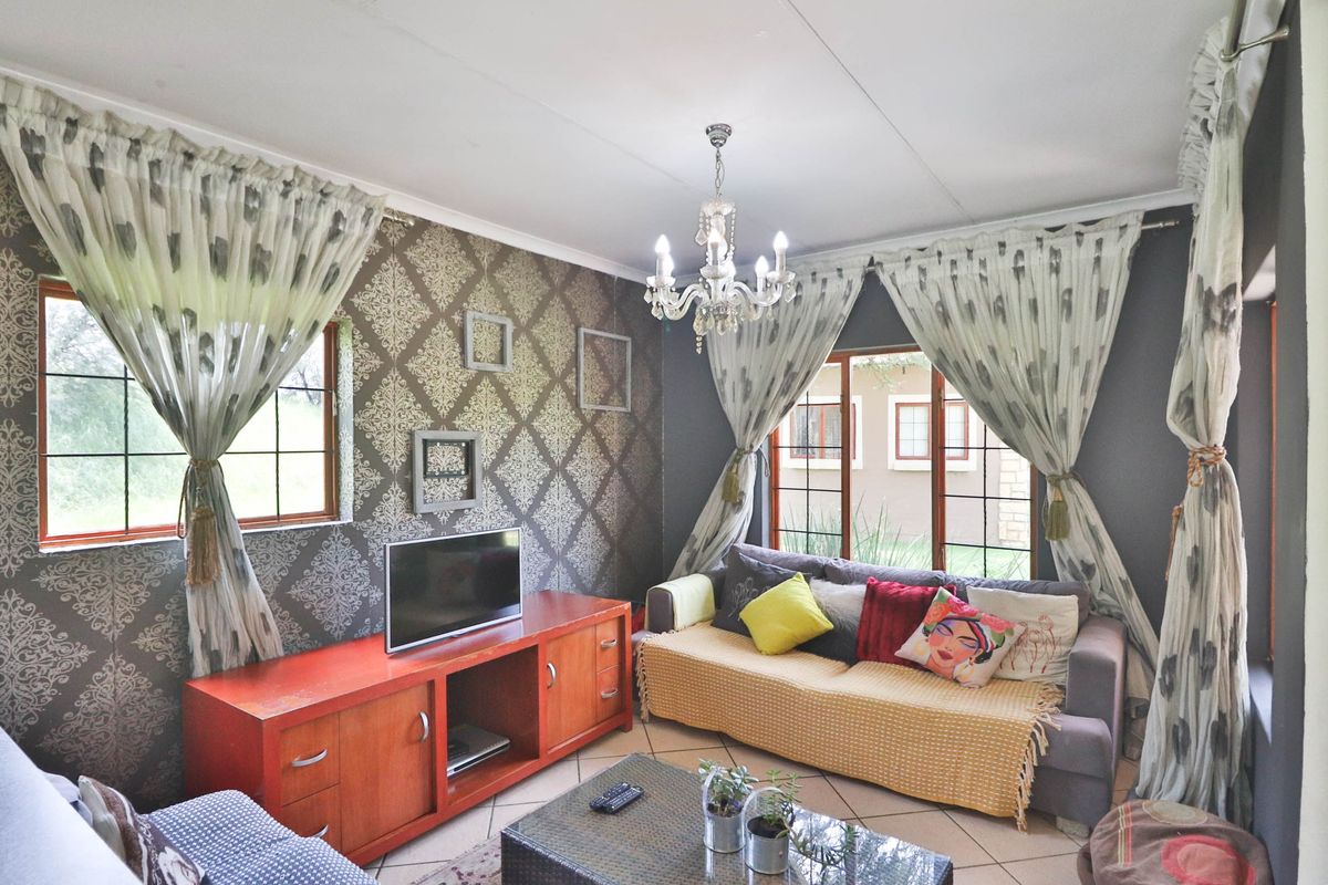 A cozy living room featuring tiled flooring, a decorative chandelier, and large windows that provide natural light.