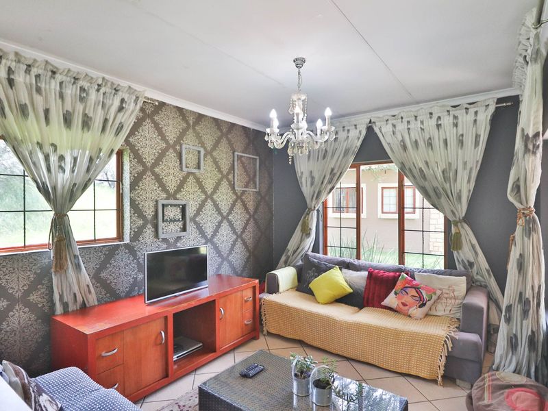 A cozy living room featuring tiled flooring, a decorative chandelier, and large windows that provide natural light.