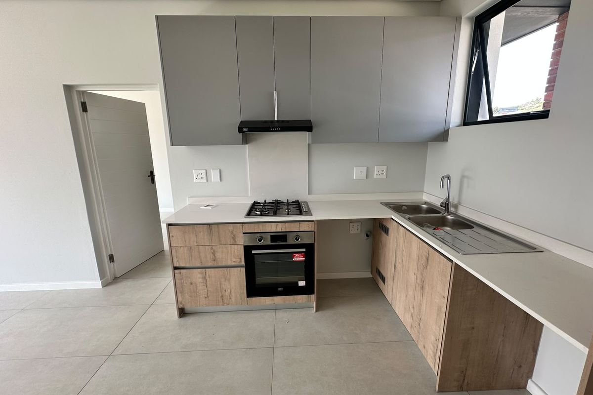 Modern kitchen featuring light wood-grain lower cabinets, grey upper cabinetry, stone countertops, integrated gas hob, oven, and a double sink with tiled flooring.