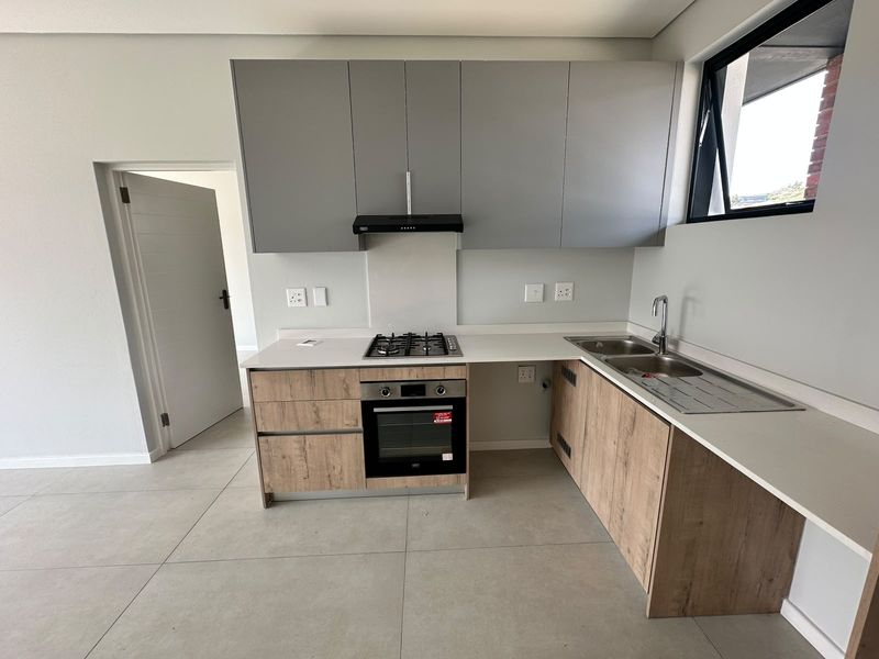 Modern kitchen featuring light wood-grain lower cabinets, grey upper cabinetry, stone countertops, integrated gas hob, oven, and a double sink with tiled flooring.