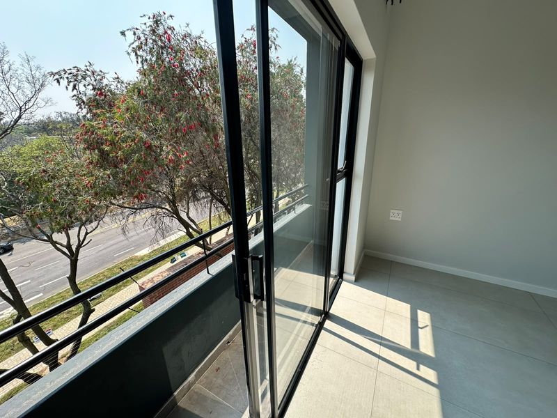 A bright, modern balcony with tiled flooring, a sleek metal railing, and large sliding glass doors offering an elevated view of the street.