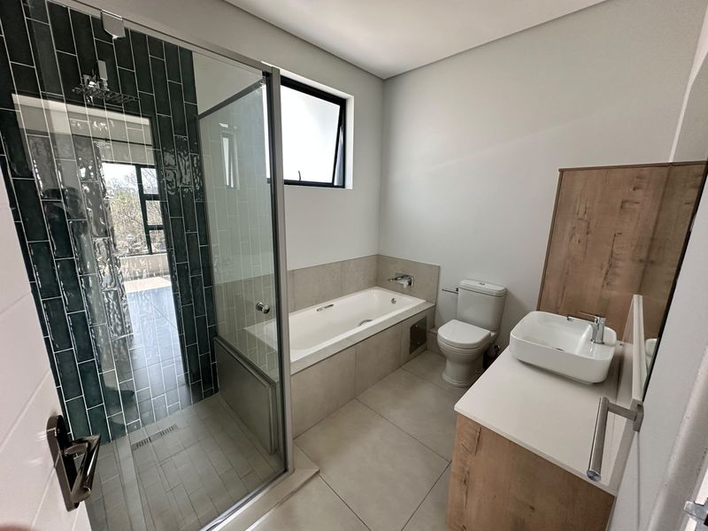 Modern bathroom featuring a glass-enclosed shower, built-in bathtub, vessel sink vanity, and contemporary tile finishes in a clean, well-maintained space.