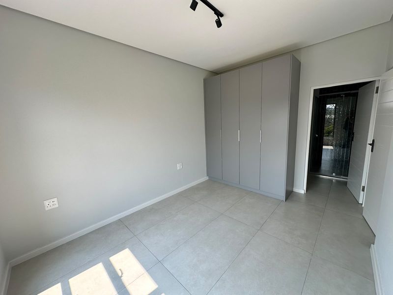 A clean, modern bedroom featuring neutral grey walls, large format floor tiles, and a built-in wardrobe with contemporary finishes.