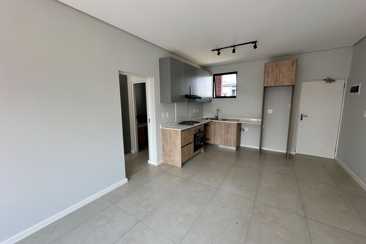 Modern open-plan kitchen featuring contemporary wood-finish cabinetry, stone countertops, integrated gas hob, oven, and extractor fan, set against neutral tiled flooring.