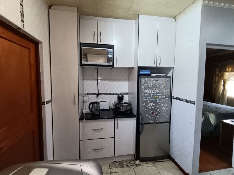 A compact kitchen area featuring white built-in cabinetry, a built-in microwave, tiled wall finishes, and a dark laminate countertop.