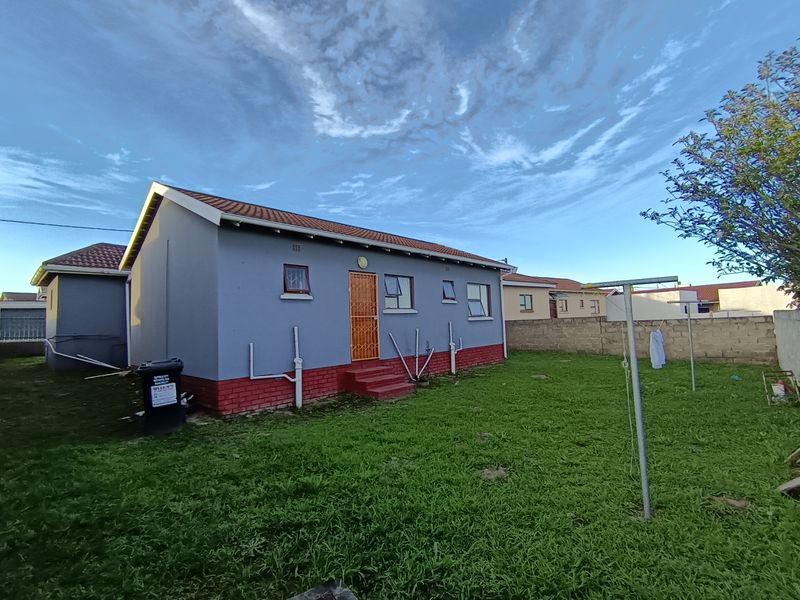 Rear view of the property featuring a lawn, brick boundary wall, and exterior access door with security gate.