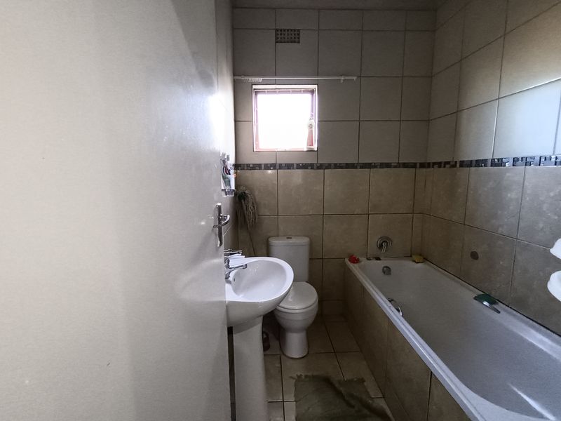 A functional bathroom featuring a pedestal basin, toilet, and bathtub with tiled walls and flooring.