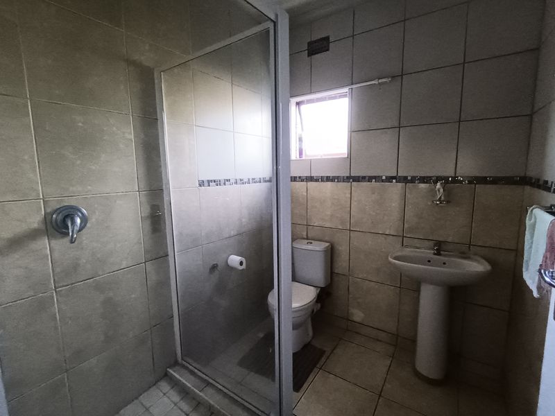 A functional bathroom featuring a pedestal basin, toilet, and a glass-enclosed shower with neutral wall and floor tiling.