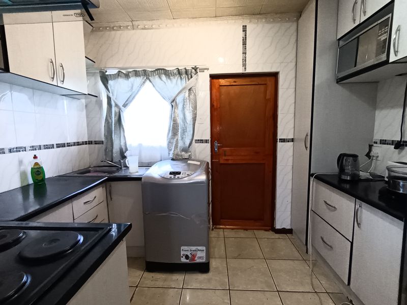 A functional kitchen featuring built-in cabinetry, laminate countertops, a tiled backsplash, and integrated appliances, providing a practical workspace with direct exterior access.