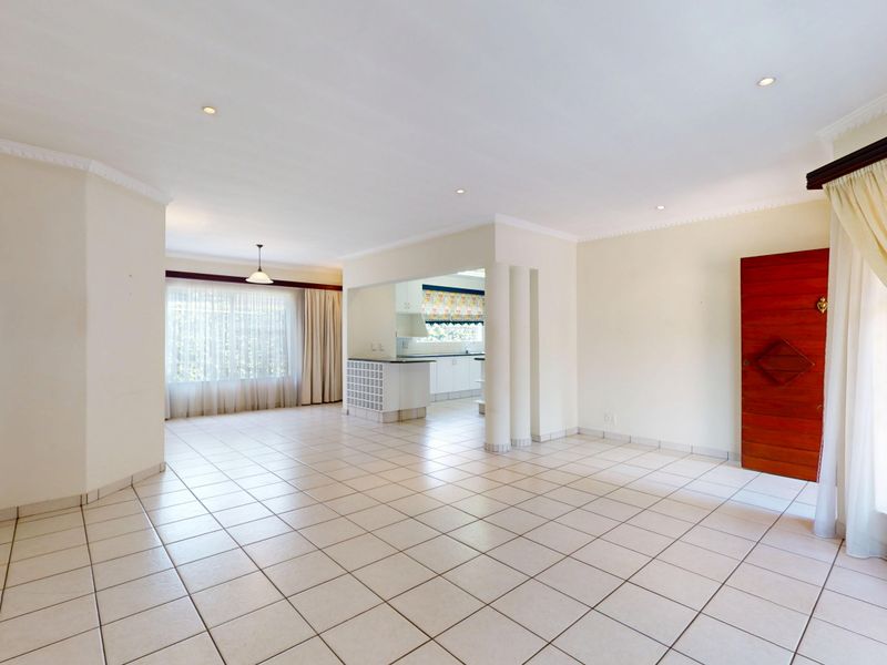 Spacious open-plan living area featuring neutral tiled flooring, recessed lighting, crown molding, and a semi-open kitchen with built-in cabinetry and a breakfast counter.