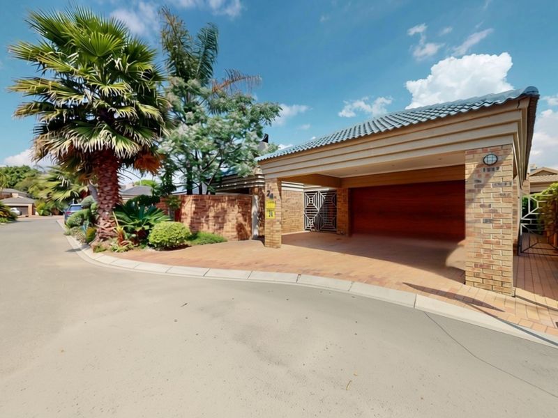 Front exterior view of the property featuring a paved driveway, covered garage, and established garden with brick boundary walling.