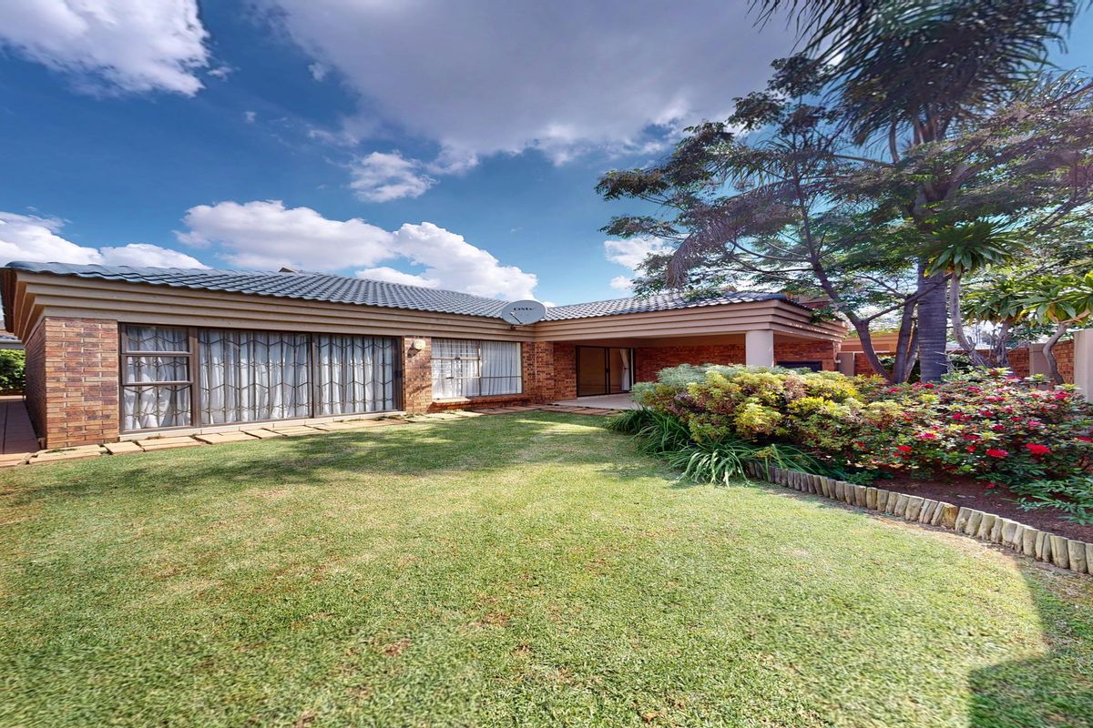 A well-maintained rear exterior view featuring a brick facade, covered patio area, and a landscaped garden with mature trees.