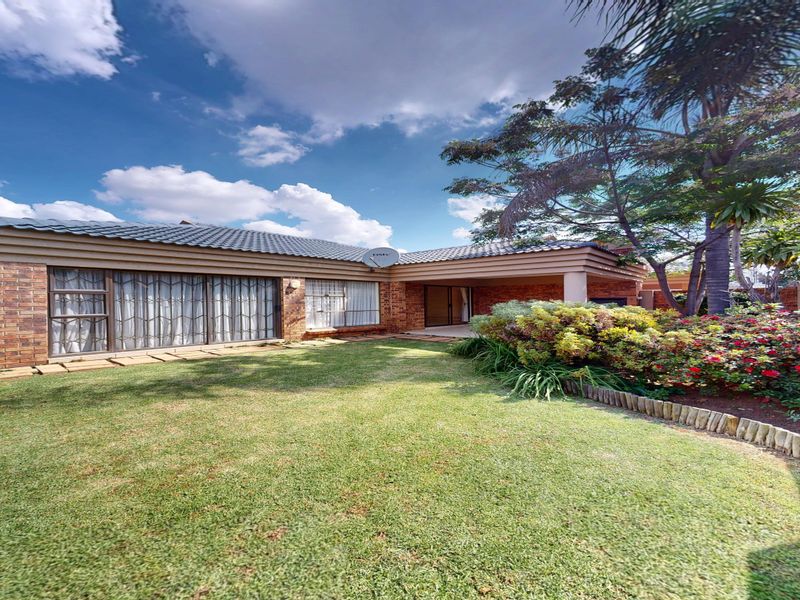 A well-maintained rear exterior view featuring a brick facade, covered patio area, and a landscaped garden with mature trees.