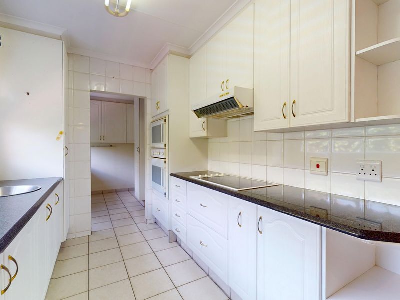 A functional kitchen featuring white cabinetry, granite countertops, tiled backsplash, and built-in appliances, with an adjacent scullery area.