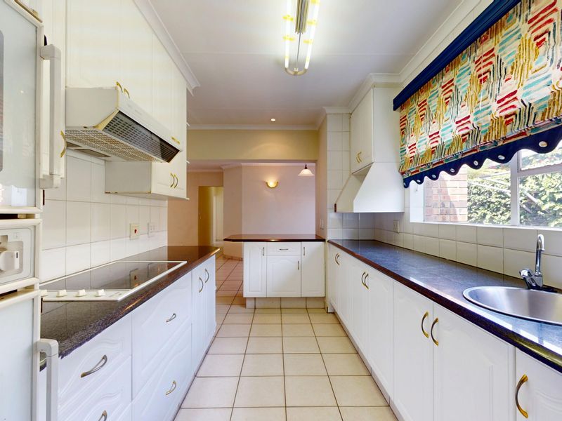 A functional galley-style kitchen featuring white cabinetry, dark countertops, an electric hob, and a stainless steel sink with tiled flooring.