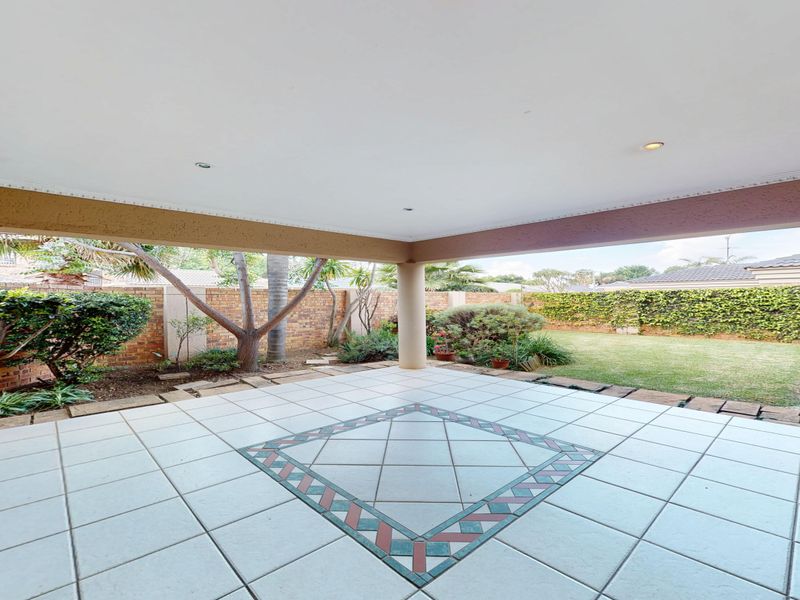 Spacious covered patio featuring tiled flooring with decorative inlay, a built-in braai, and direct access to the private garden area.