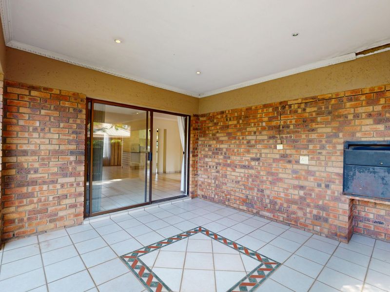 Covered patio area featuring exposed brick walls, tiled flooring with decorative inlay, and a built-in braai, providing direct access to the interior living space.