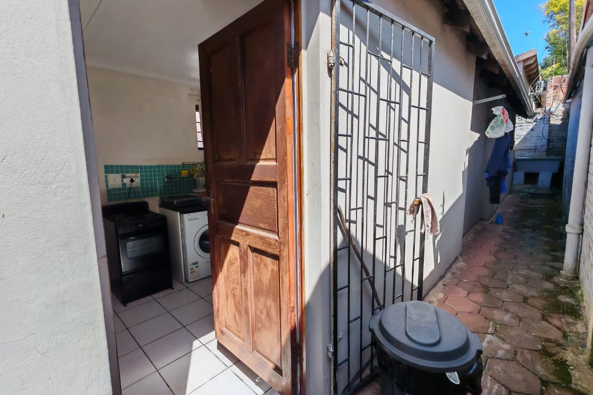 View of a kitchen entrance from an exterior paved side walkway, featuring a security gate and tiled kitchen flooring.