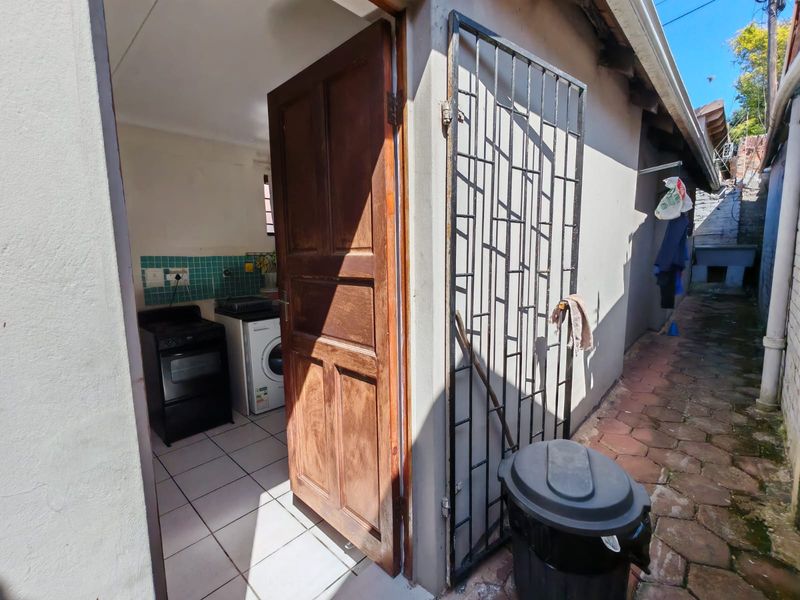 View of a kitchen entrance from an exterior paved side walkway, featuring a security gate and tiled kitchen flooring.