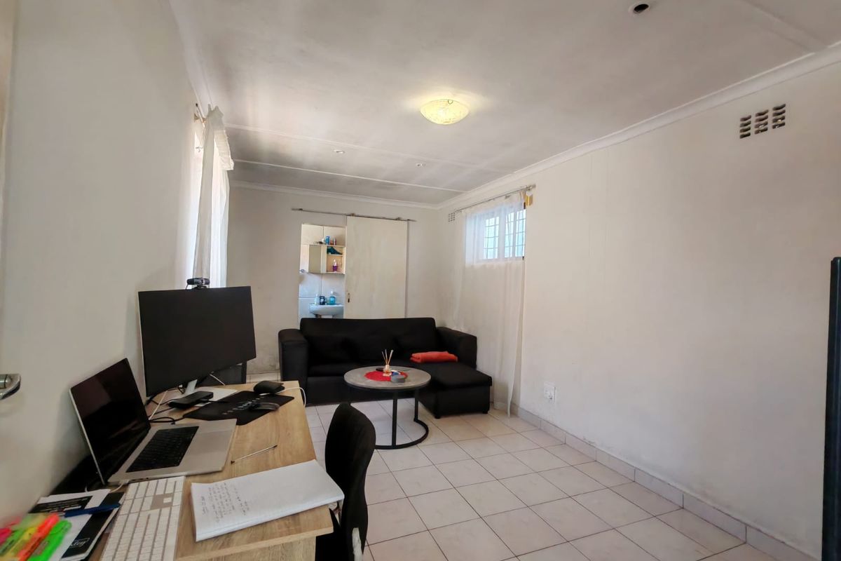 A functional living area featuring tiled flooring, a sliding door, and security bars on the window, offering a blank canvas for potential interior updates.
