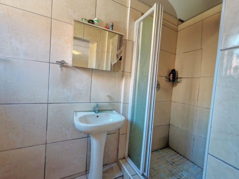A functional bathroom featuring a pedestal basin, a shower enclosure with tiled walls, and a wall-mounted medicine cabinet.