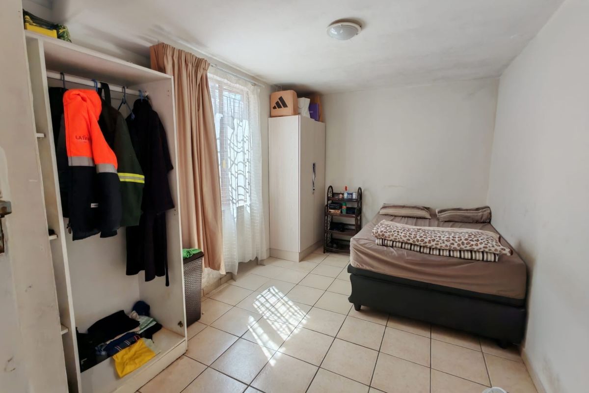 A bedroom featuring tiled flooring, a built-in wardrobe, and natural light from the window. The space requires minor cosmetic updates to improve its overall condition.