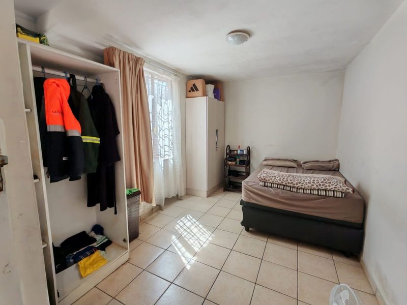 A bedroom featuring tiled flooring, a built-in wardrobe, and natural light from the window. The space requires minor cosmetic updates to improve its overall condition.