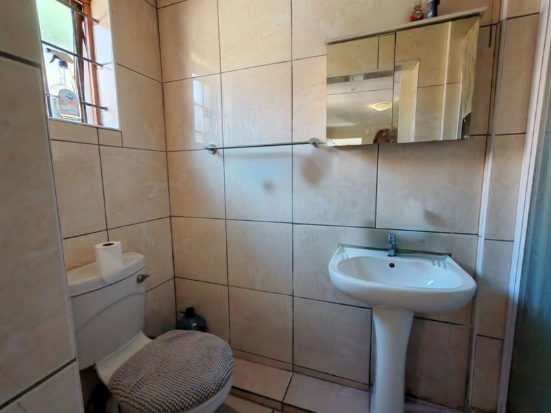 A functional bathroom featuring floor-to-ceiling wall tiles, a pedestal basin, a toilet, and a mirrored medicine cabinet.