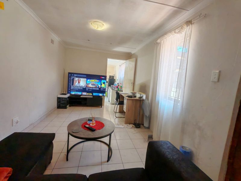 A living room area featuring tiled flooring and neutral walls, with an open-plan layout leading to the kitchen area.