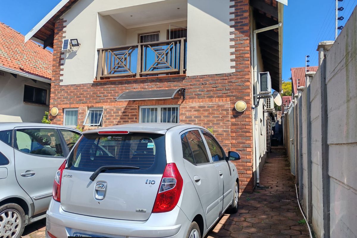 Rear exterior view of the property featuring a face brick facade, a balcony with timber balustrades, and a paved side access path.