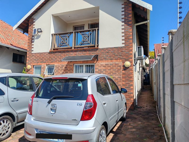 Rear exterior view of the property featuring a face brick facade, a balcony with timber balustrades, and a paved side access path.