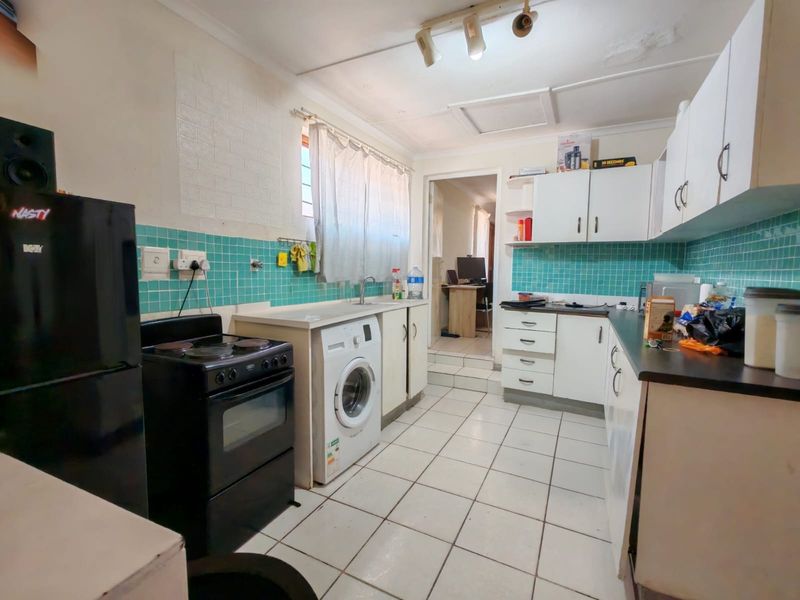 A functional kitchen featuring tiled flooring, a tiled backsplash, built-in cabinetry, and integrated plumbing for laundry appliances, requiring some cosmetic updates.