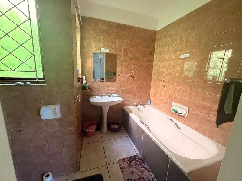 A dated bathroom featuring a pedestal basin, built-in bathtub, and full-height wall tiling, offering potential for a modern renovation.