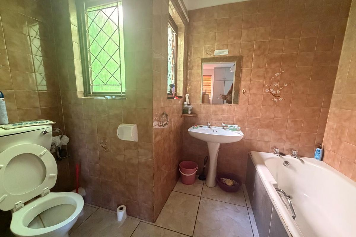 A dated bathroom featuring a pedestal basin, built-in bathtub, and full-height ceramic wall tiling, requiring cosmetic updates to modernize the space.