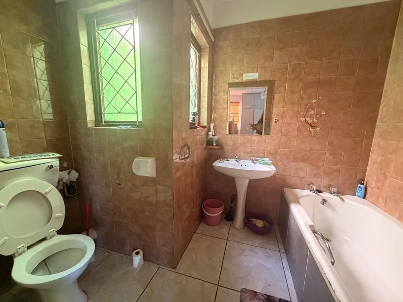 A dated bathroom featuring a pedestal basin, built-in bathtub, and full-height ceramic wall tiling, requiring cosmetic updates to modernize the space.