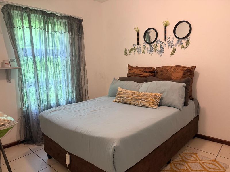 A standard bedroom featuring tiled flooring and a window with sheer curtains, providing a functional and neutral living space.