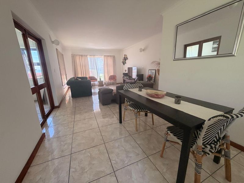 An open-plan living and dining area featuring neutral tiled flooring, a sliding glass door providing natural light, and classic cove cornicing.