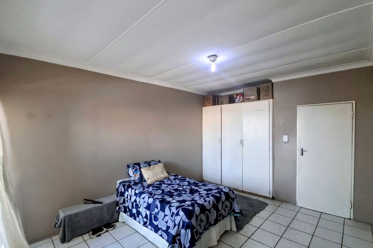A functional bedroom featuring tiled flooring, built-in cupboards, and neutral wall finishes, providing a practical and well-maintained living space.