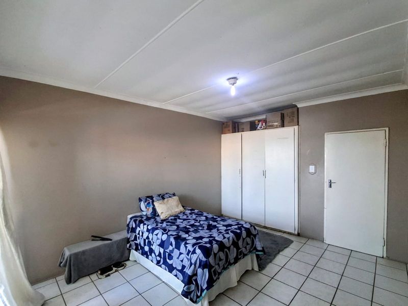 A functional bedroom featuring tiled flooring, built-in cupboards, and neutral wall finishes, providing a practical and well-maintained living space.