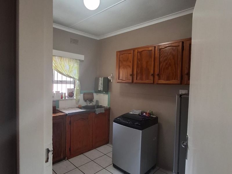 A functional kitchen featuring built-in wooden cabinetry, tiled flooring, and a tiled splashback, offering a practical layout with potential for modern updates.