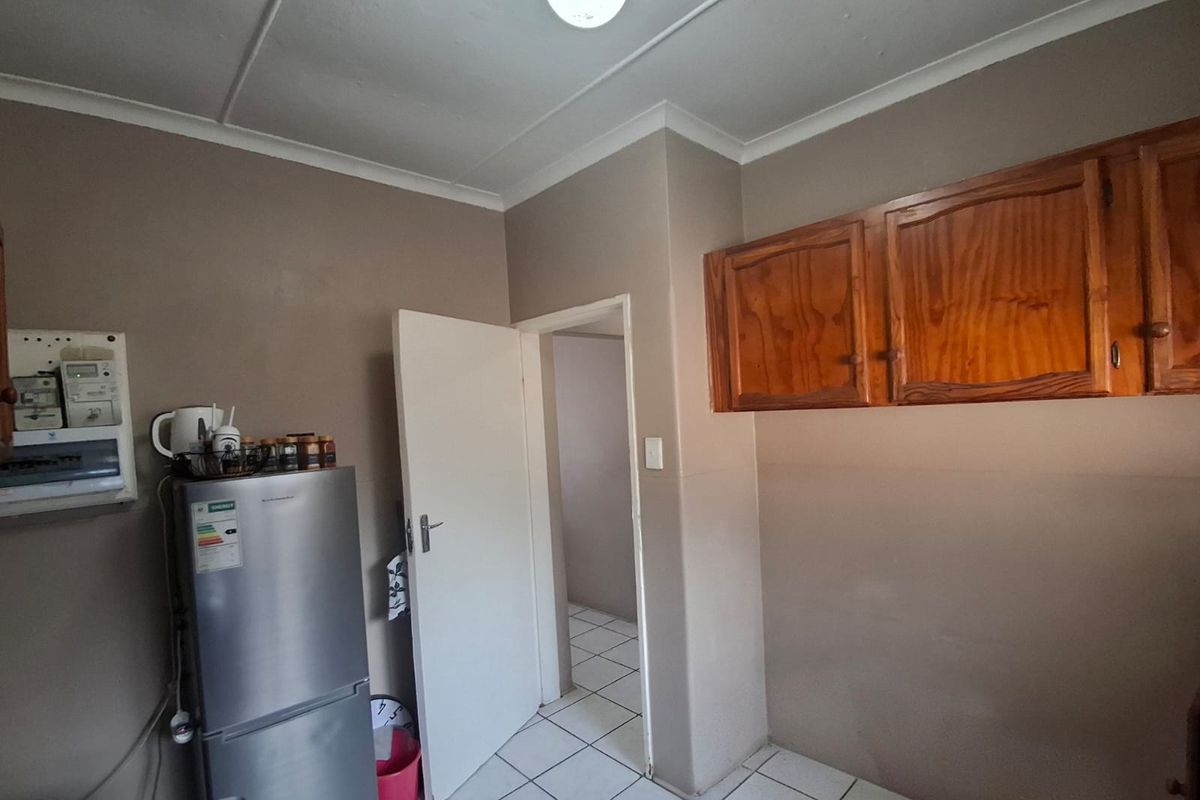 A functional kitchen area featuring tiled flooring, built-in wooden wall cabinetry, and a standard electrical distribution board.