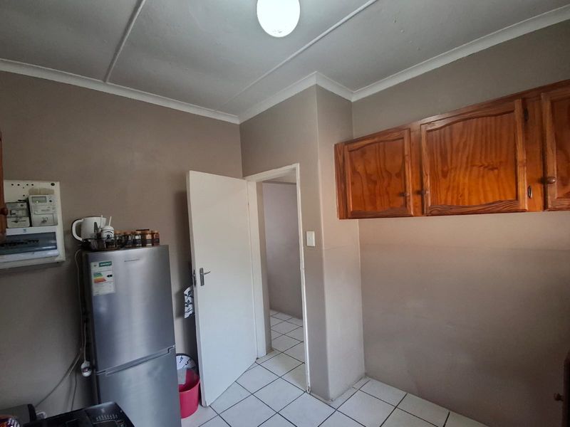 A functional kitchen area featuring tiled flooring, built-in wooden wall cabinetry, and a standard electrical distribution board.