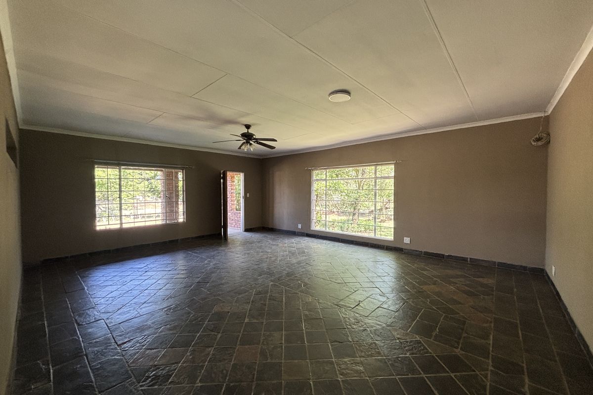 Spacious, empty living area featuring traditional slate tile flooring, a ceiling fan, and large windows with security bars, offering a blank canvas for interior design.