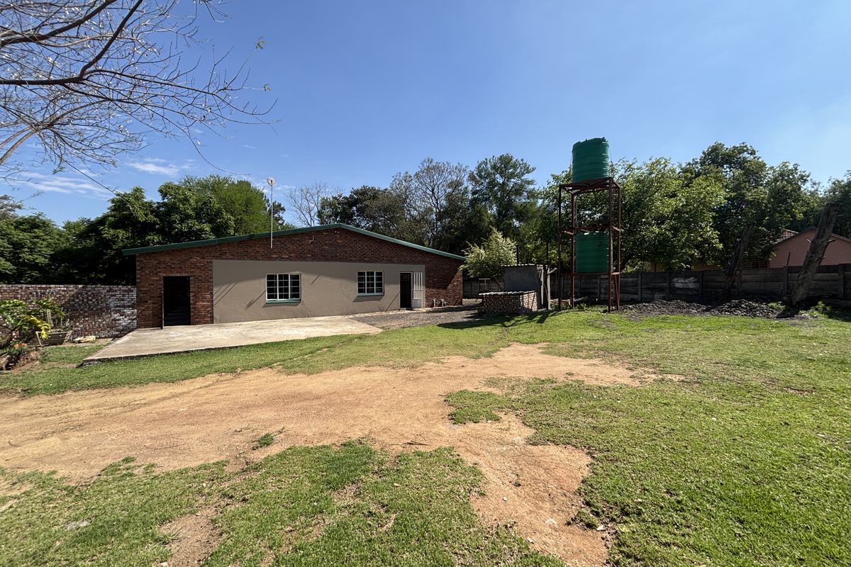 Rear view of the property featuring a brick and plastered exterior, concrete patio area, and elevated water storage tanks set within a large garden.