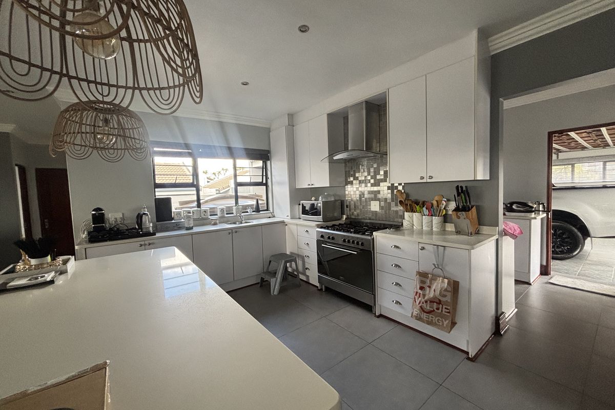 Modern kitchen featuring white cabinetry, a central island, stainless steel oven with extractor fan, tiled backsplash, and large floor tiles.