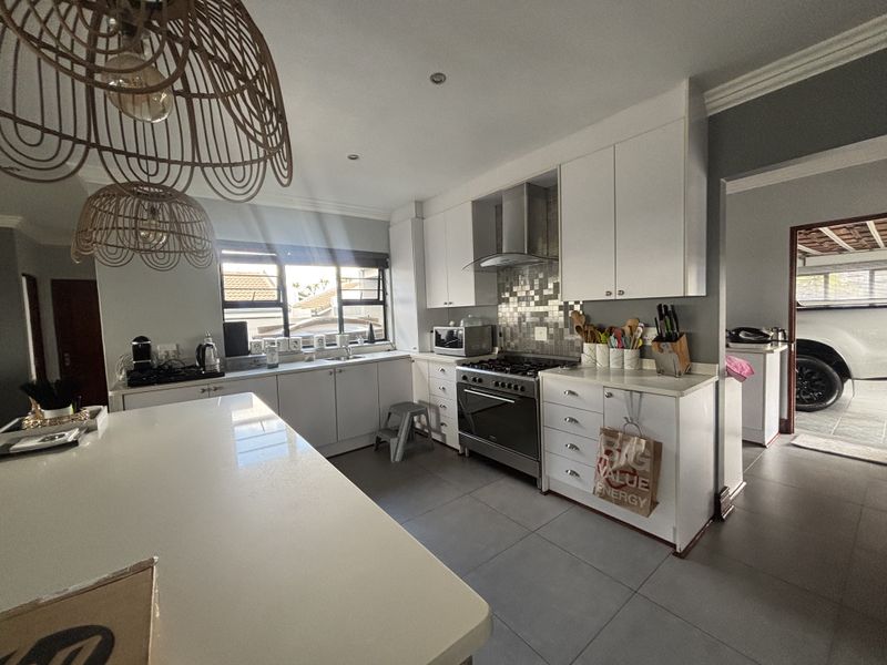 Modern kitchen featuring white cabinetry, a central island, stainless steel oven with extractor fan, tiled backsplash, and large floor tiles.