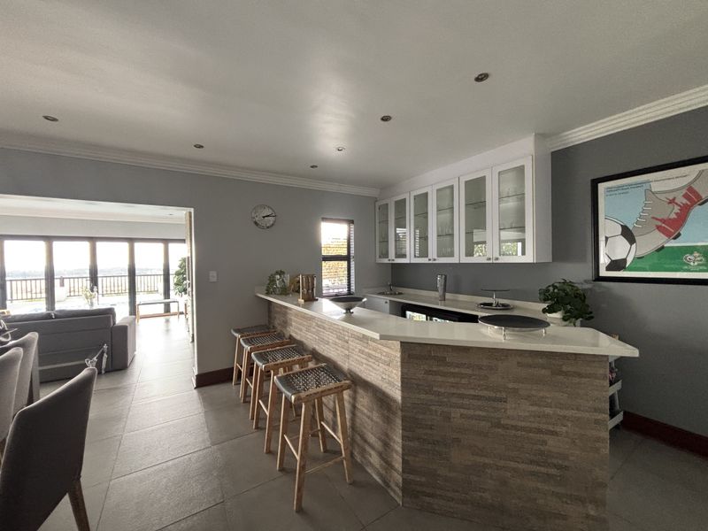 A well-appointed home bar area featuring a stone-clad counter, glass-fronted cabinetry, and recessed lighting, seamlessly connected to the adjacent living space.